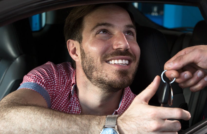 Smiling man inside a car receiving keys
