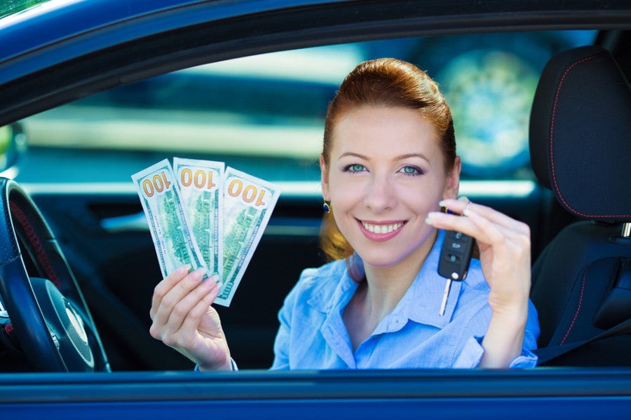 Smiling woman in a car holding cash and car keys 