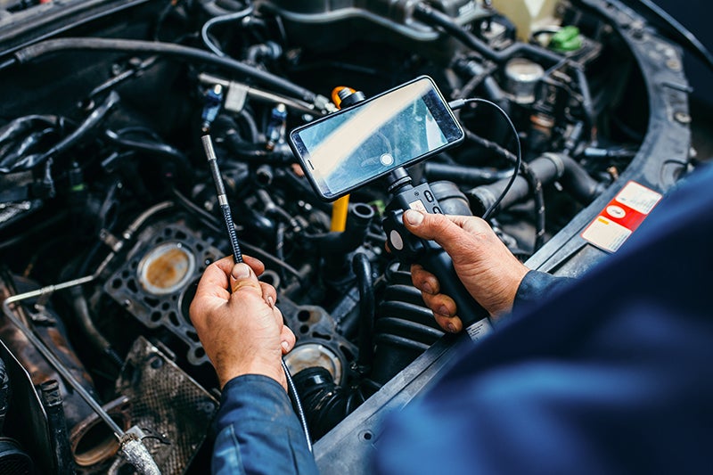 Mechanic inspecting a car engine using a borescope camera connected to a smartphone